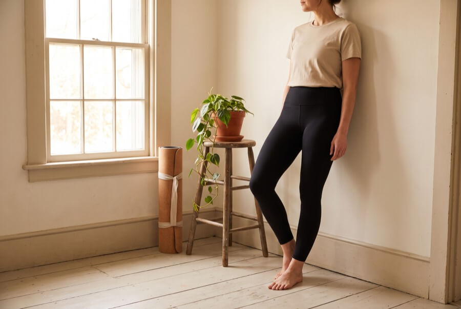 Woman wearing plain high-waisted black leggings beside a rolled yoga mat
