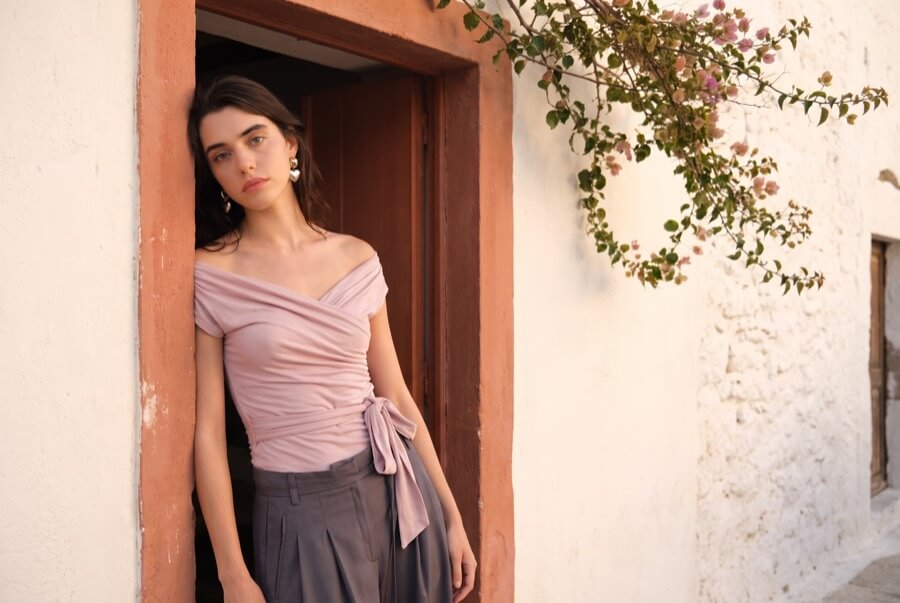 Woman wearing a dusk pink off-shoulder wrap top in a terracotta doorway