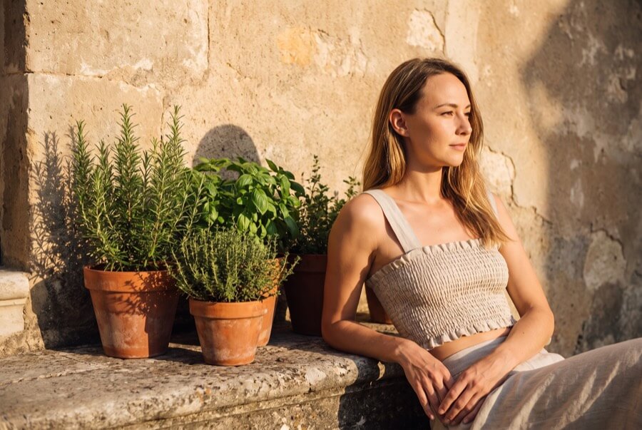 Woman wearing a natural smocked linen crop top on a sun-warmed stone step