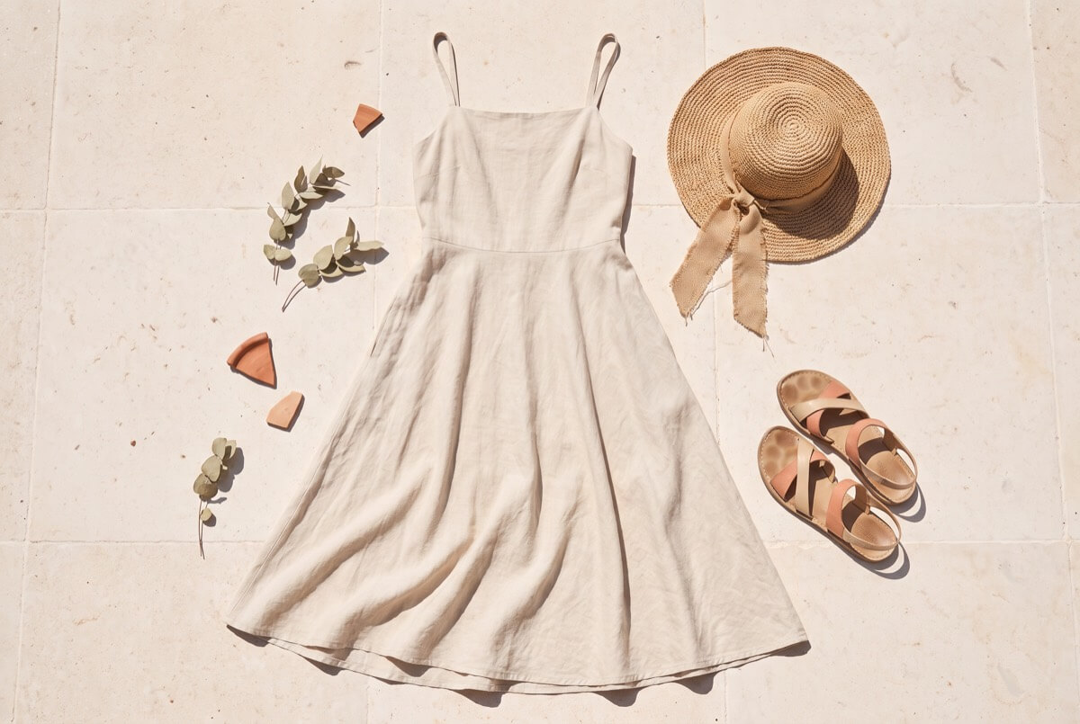 Stone-washed linen slip dress laid flat with a straw hat and sandals for a hot summer day