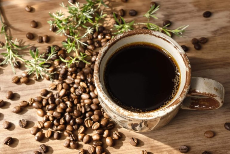 Rustic ceramic mug with coffee beans and greenery.