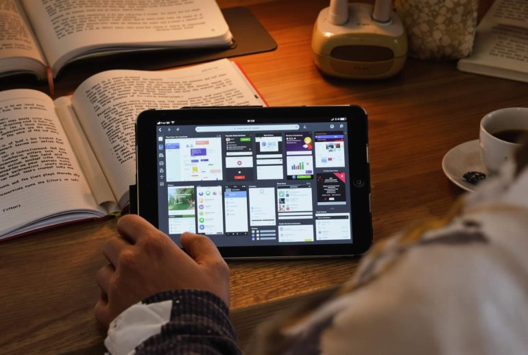 Student using tablet with study apps, surrounded by books.
