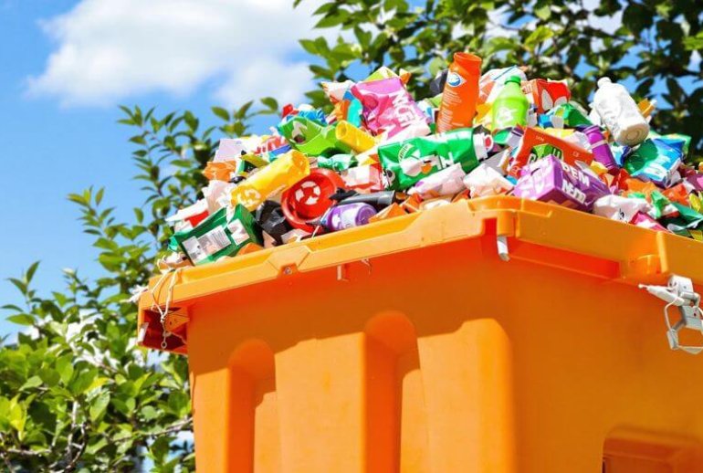 Colorful recycling bin with waste and greenery around it.